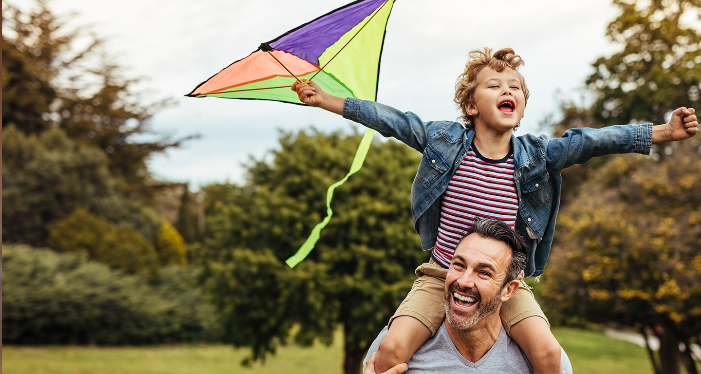 A father carrying his son on his shoulders as they fly a kite