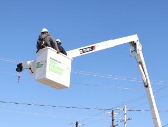 A white, electric bucket truck boom with bucket extended above power lines