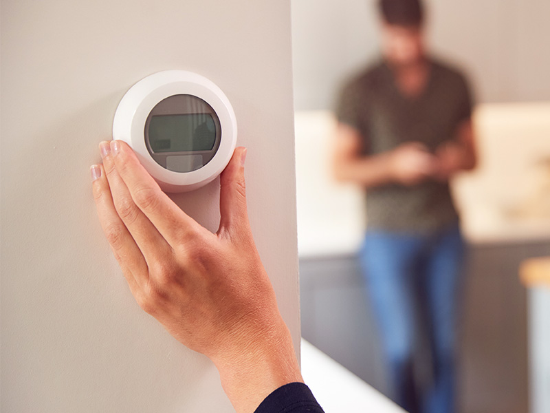 a hand adjusting a smart thermostat on the wall in a home