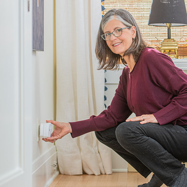 woman kneeling down to plug in a carbon monoxide detector