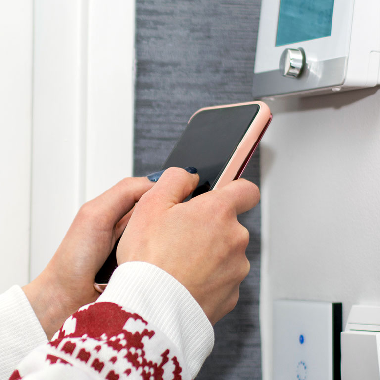 closeup of hands controlling a smart thermostat with a smartphone