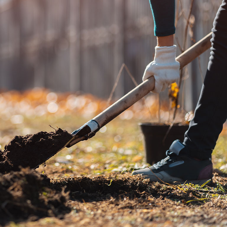 woman wearing safety gloves and boots digging a hole in the ground