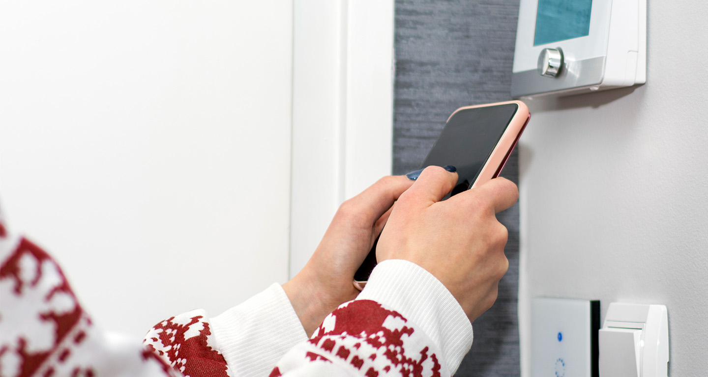 closeup of hands controlling a smart thermostat with a smartphone