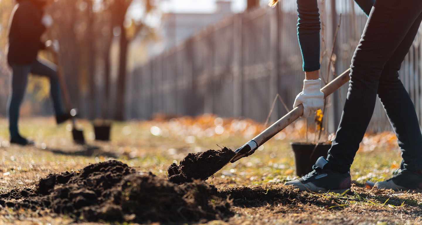 woman wearing safety gloves and boots digging a hole in the ground