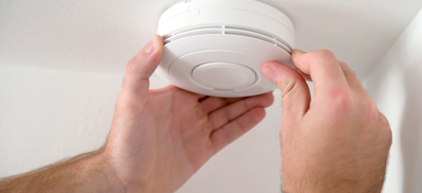 close-up of two hands opening a carbon monoxide alarm to change the battery