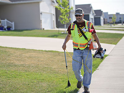 Gas technician wearing a safety vest carrying a gas leak detection device through a neighborhood