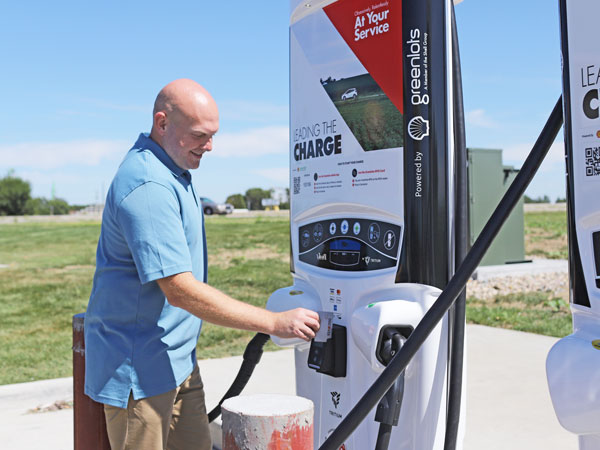 Man wearing a blue shirt and khaki pants swiping a credit card at an electric vehicle charging station